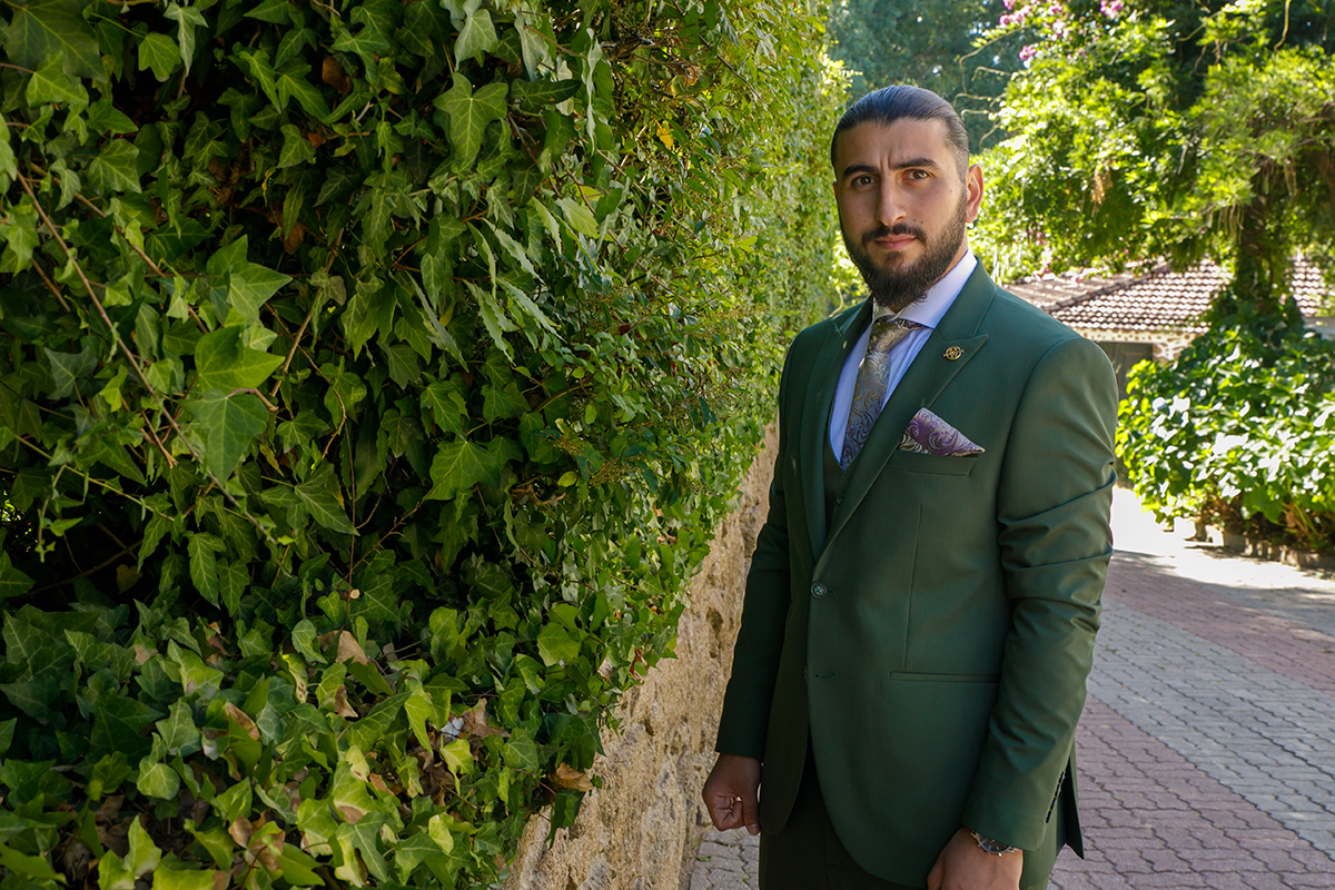 Furkan encostado a um muro de trepadeiras e pedra, com um olhar sério para a câmara de Ricardo Coimbra Fotografia.