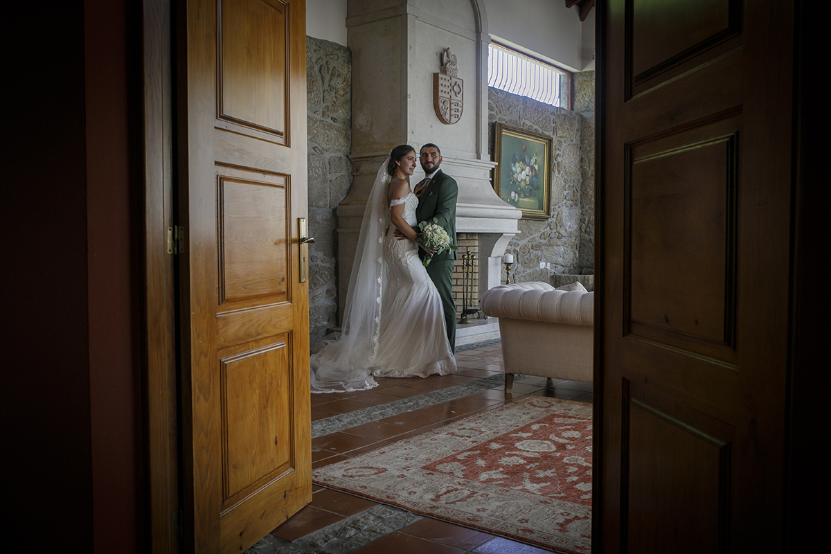 Através da porta aberta, os noivos junto à lareira, num momento íntimo.