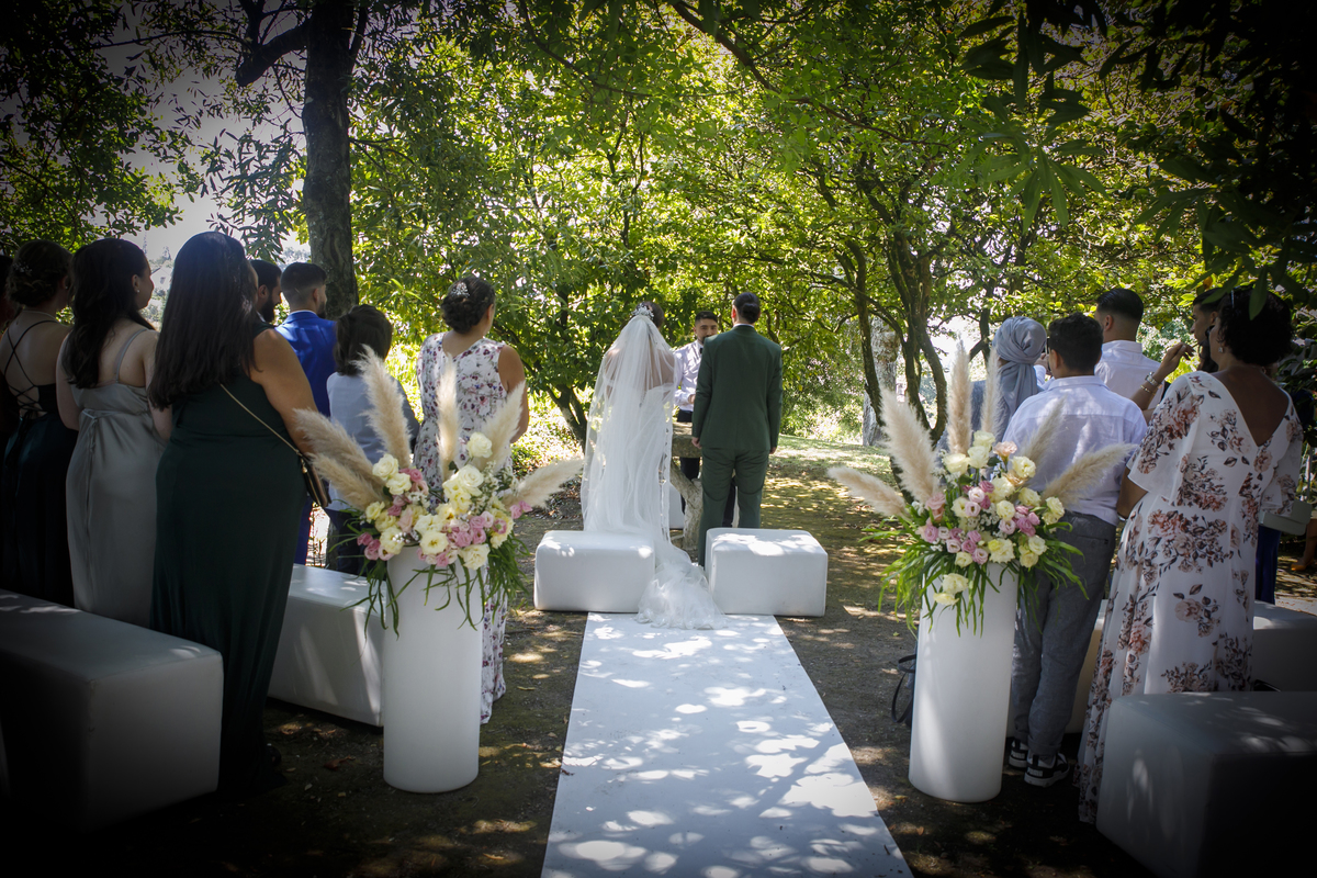 A caminho do altar, foto vinhetada dos noivos e convidados de costas, ao ar livre com passadeira branca. Reportagem casamento