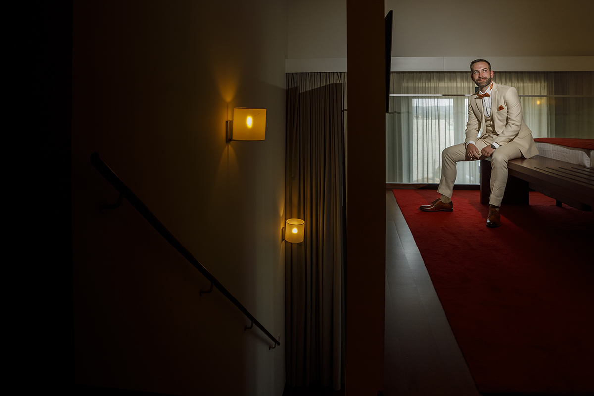  A luz é escassa, mas o sentimento é imenso. O noivo está sentado na cama, pensativo, com os pés sobre uma carpete vermelha. Do outro lado, as escadas iluminadas por candeeiros criam uma dualidade entre a reflexão interior e a beleza do ambiente.