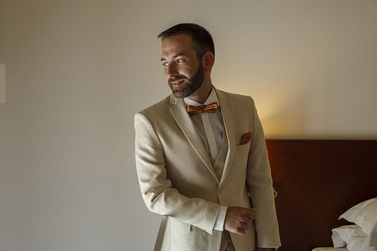 Num retrato sereno da cintura para cima, Mathieu olha para a luz que entra pela janela com um sorriso confiante. A parede branca e a cabeceira de madeira criam o cenário perfeito para um momento de introspeção antes do grande passo.