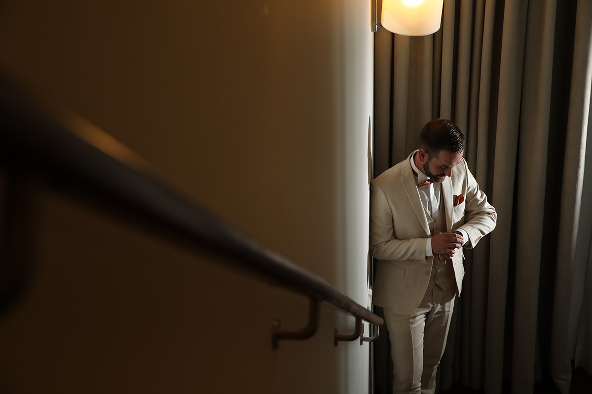 Ao pé do corrimão rústico, o noivo ajusta o relógio com atenção. O gesto revela a emoção do tempo a aproximar-se, enquanto se prepara com elegância para um dos momentos mais importantes da sua vida.