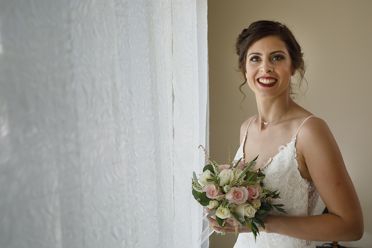 Agora com um sorriso cheio de luz, Marta segura o seu bouquet e olha para a câmara. O fundo suave reforça a sua beleza serena, num momento onde tudo parece em paz.