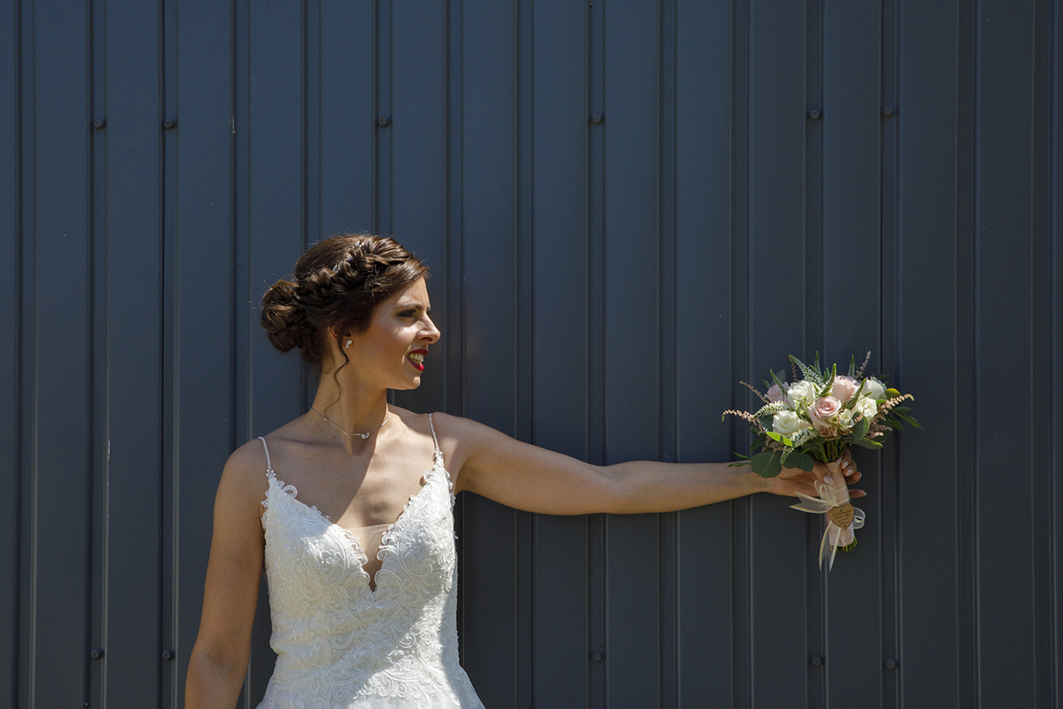 Junto à parede escura, Marta estende o braço com o bouquet. O seu olhar é dirigido às flores, um gesto simples que espelha felicidade e orgulho.