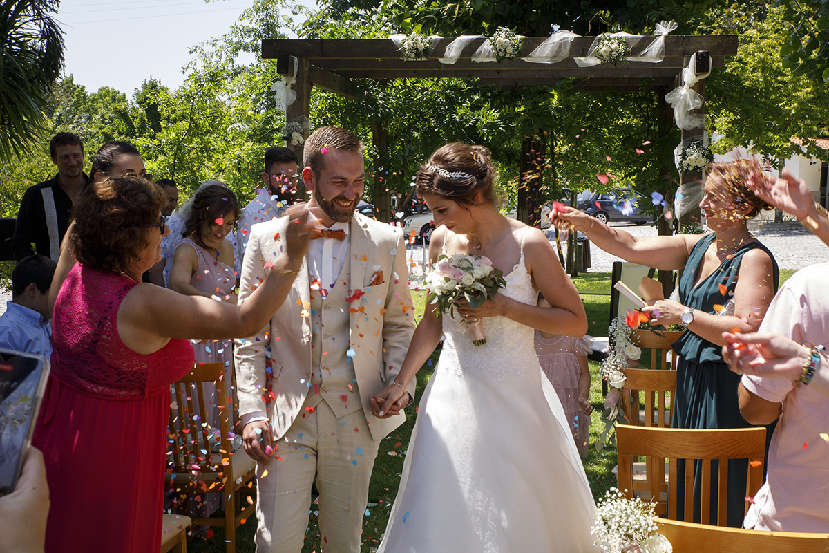 quinta dos compadres .Entre os convidados, pétalas de rosa voam no ar. Marta e Mathieu caminham lado a lado sob uma chuva de cores e alegria, numa imagem vibrante de felicidade.