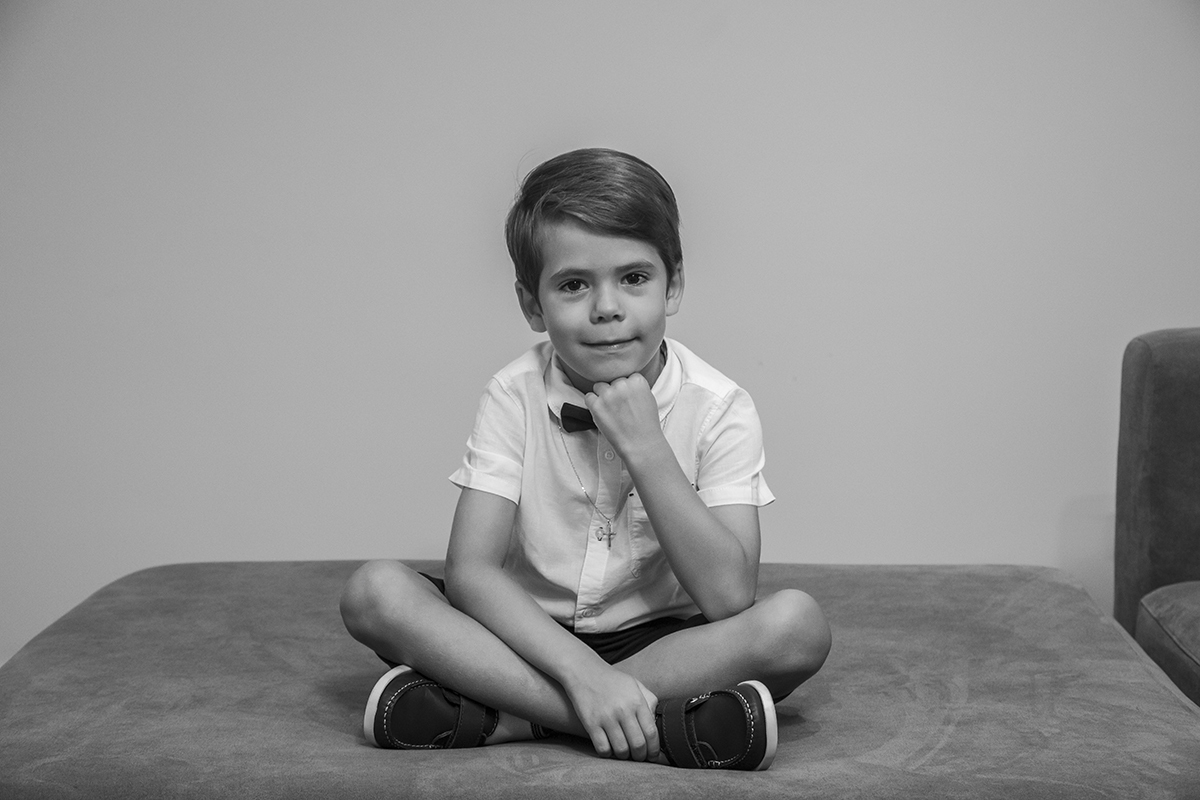 Sentado confortavelmente no sofá, com as pernas cruzadas, uma mão junto ao sapato e o punho a apoiar o queixo, Ethan surge sério, mas feliz. Esta imagem a preto e branco mostra um momento de pausa e reflexão.