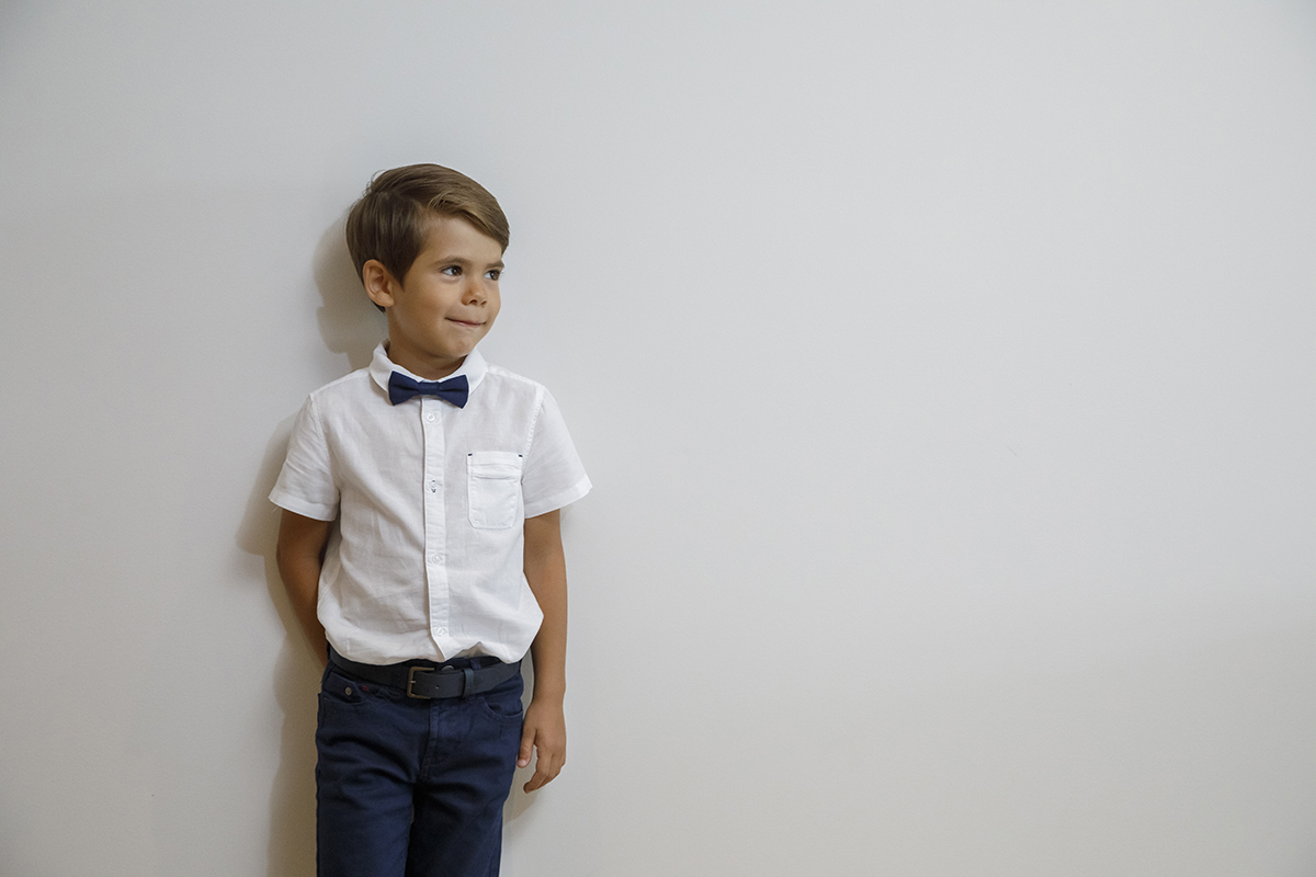 Ethan encosta-se a uma parede branca, numa composição harmoniosa e simples. A pose descontraída, uma mão ao lado e outra atrás das costas, combina com o seu sorriso leve, tornando esta fotografia uma verdadeira pintura de serenidade.