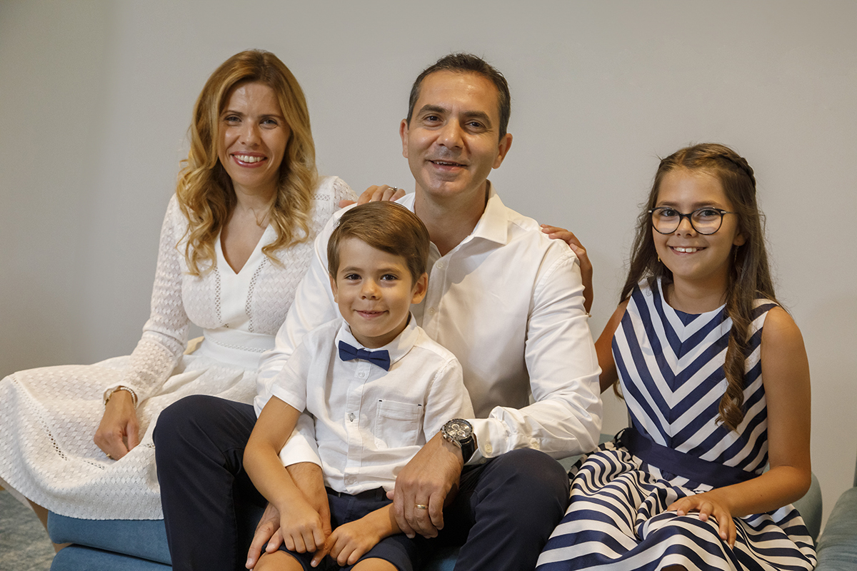 Um retrato familiar cheio de harmonia: a mãe do lado esquerdo, o pai ao centro com Ethan ao colo, e a irmã do lado direito. Sorrisos genuínos revelam o amor e a união de uma família verdadeiramente feliz.