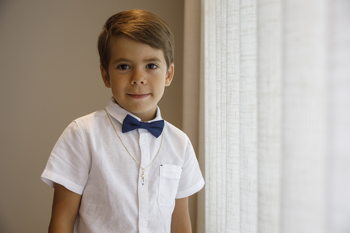 Num retrato dos cotovelos para cima, Ethan encara a câmara com um sorriso subtil. O seu laço azul e o fio dourado completam este momento elegante, marcado por inocência e charme.