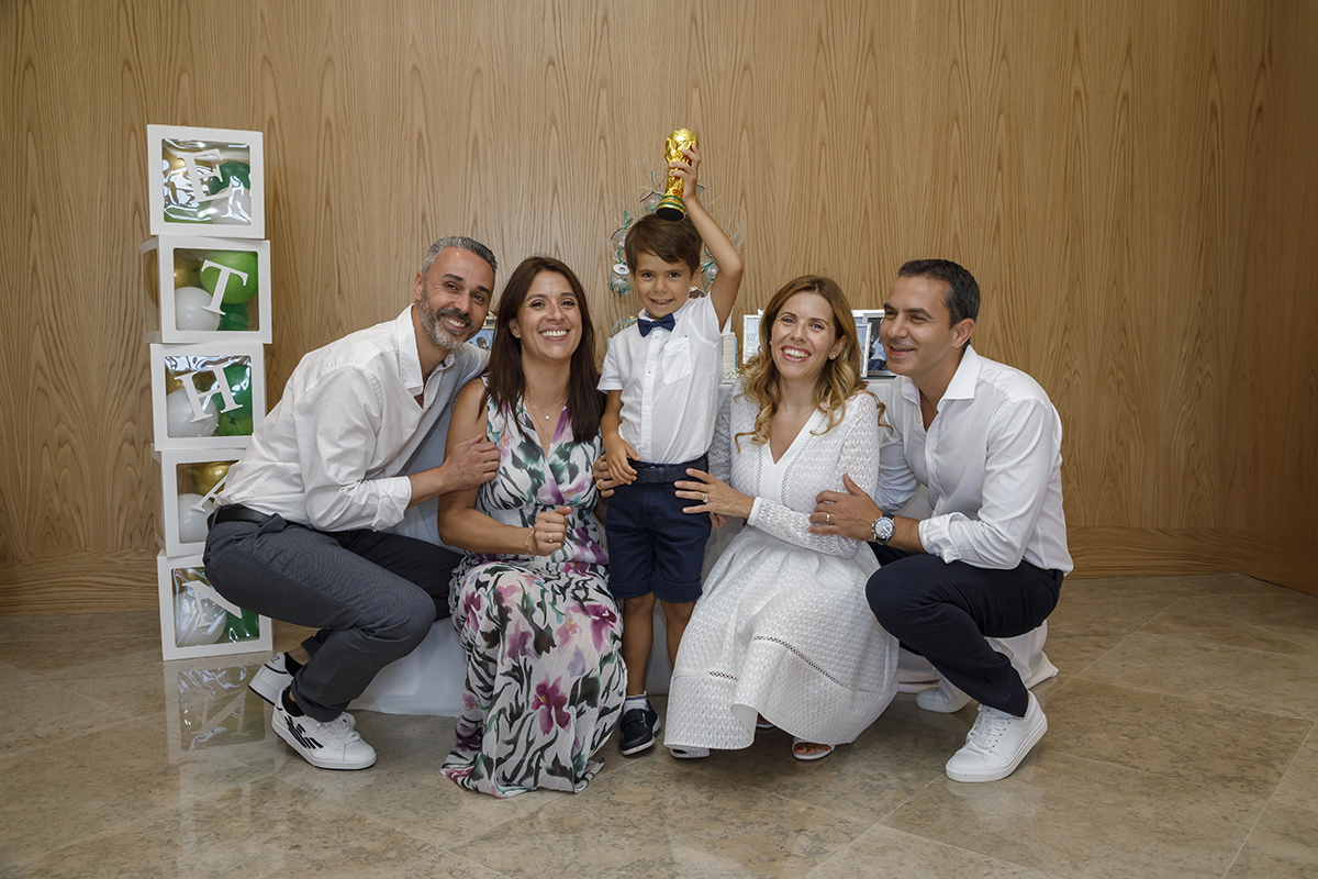 Uma composição divertida e cheia de espírito: ao lado de uma torre de cubos fotográficos, Ethan levanta um troféu com orgulho, rodeado pelos tios e pelos pais. Sorrisos largos e alegria contagiante, um final perfeito para um dia inesquecível.