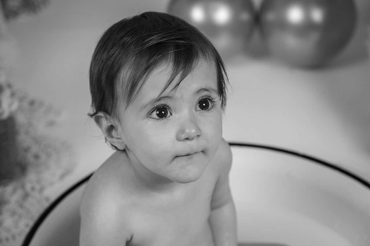 Em preto e branco, vemos Matilde num plano contrapicado, a olhar séria para cima. Está sem roupa, dentro de uma bacia branca, e o fundo desfocado reforça a simplicidade e doçura da imagem.