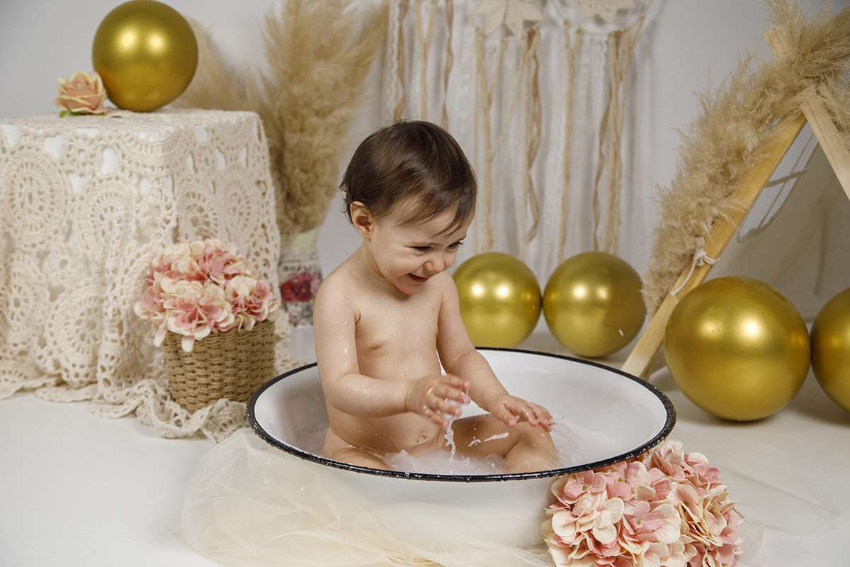 Aqui, Matilde olha para baixo e sorri com entusiasmo após chapinhar na água. O momento mostra a sua diversão pura, com as mãos ainda dentro da bacia e gotas de água visíveis.