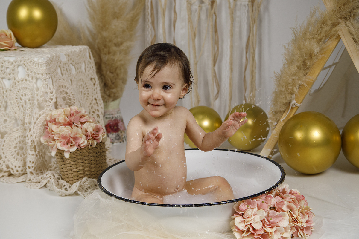 Sessao bébé estudio. Matilde, com um sorriso espontâneo, olha para a esquerda com as mãos no ar após chapinhar na água. Um momento divertido e leve, captado com toda a naturalidade e encanto.