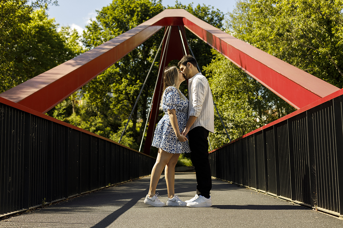Abraçados de mãos dadas, partilham um beijo terno no meio da ponte.