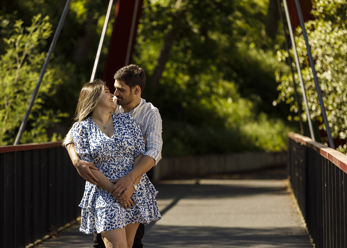 Através das grades da ponte, Luís abraça Márcia por trás. Olham-se com ternura.