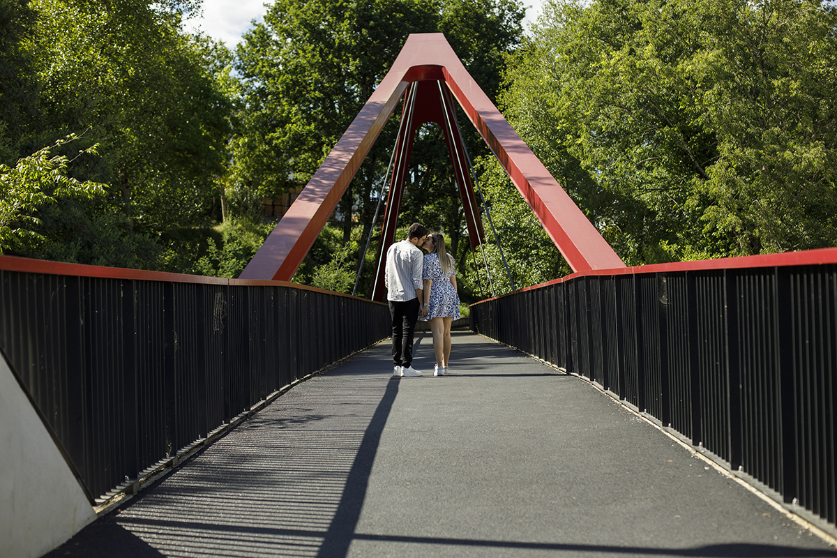 Ao fundo da ponte, vistos de costas, beijam-se, irradiando felicidade.