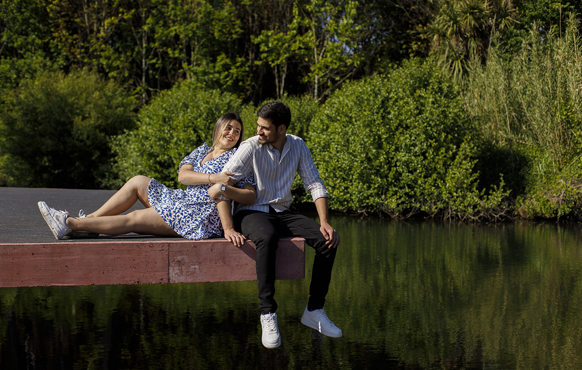 Numa estrada elevada, o rio corre abaixo. Luís e Márcia trocam um olhar terno, rodeados pela natureza.