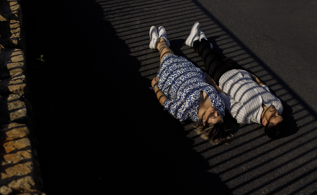 Deitados no alcatrão, sombras das grades desenham padrões sobre eles, criando uma composição artística.