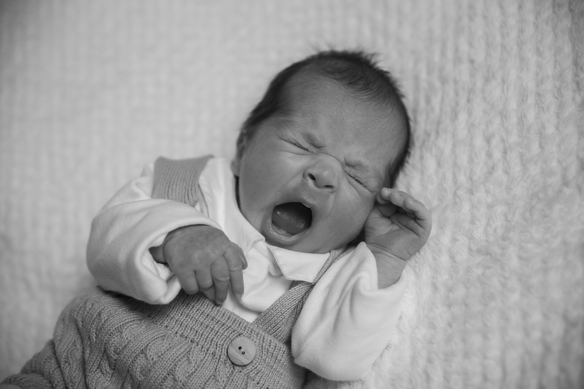 Aqui, a preto e branco, vemos Gabriel deitado, com uma das mãos junto à carinha e outra no peito, com a boca entreaberta como se estivesse a espreguiçar-se ou prestes a sorrir. fotografia recem nascido