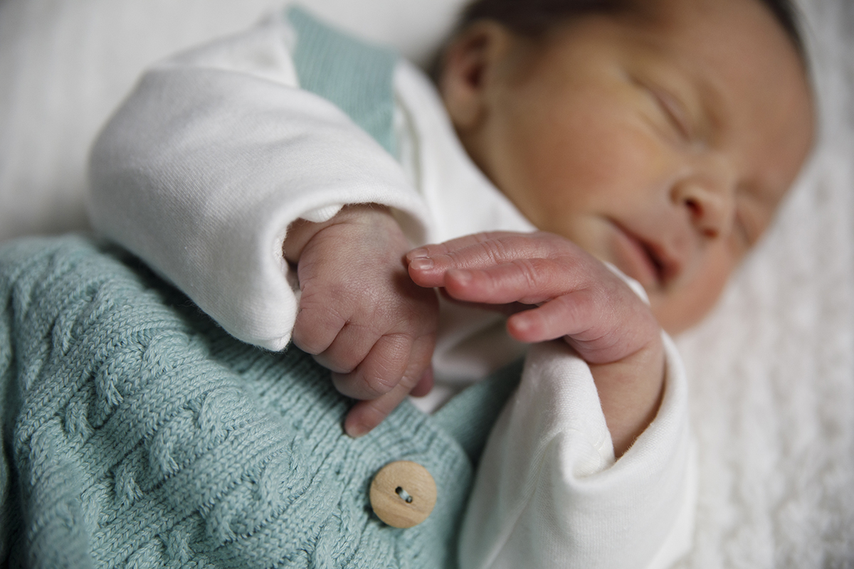 Um enquadramento mais próximo de Gabriel a dormir, com destaque nas mãos e na sua roupa delicada. O fundo está desfocado, reforçando o foco no bebé.