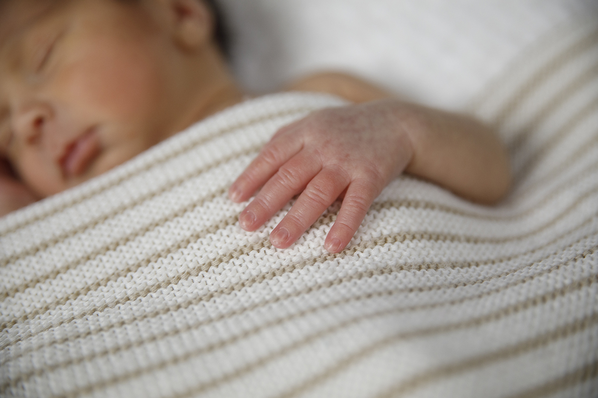 Um plano de detalhe onde vemos em foco a mantinha branca às riscas castanhas e a pequena mãozinha de Gabriel. O rosto está desfocado, dando protagonismo aos pormenores.