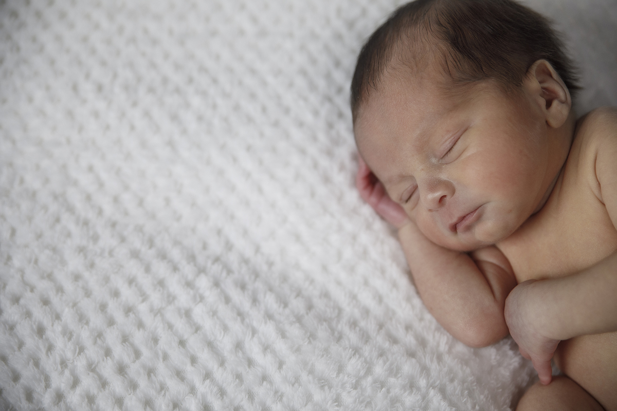 Gabriel aparece deitado no lado direito da foto, sem roupa, com uma mão sobre o peito e outra debaixo do rosto. À esquerda da imagem vê-se a sua mantinha branca.