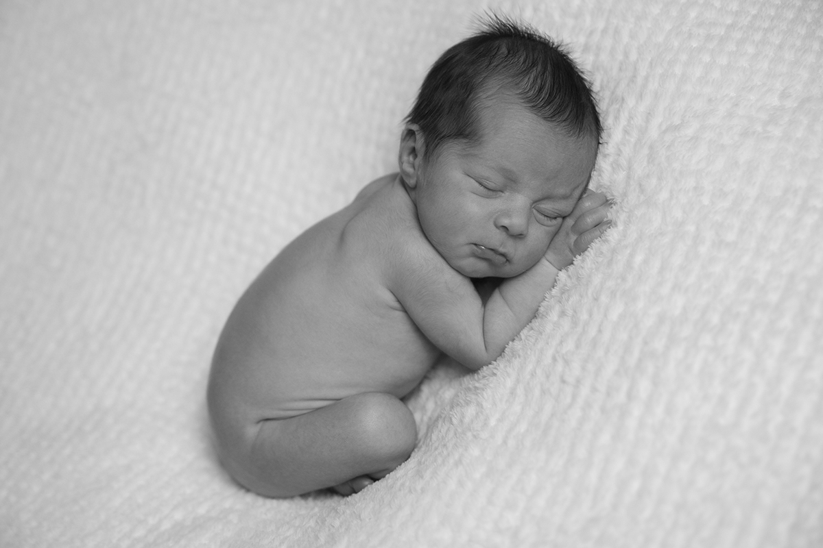 Gabriel está deitado de costas, encolhido, com as mãos esticadas à frente e a cabecinha pousada sobre elas. A imagem é em preto e branco, reforçando a suavidade do momento. Sessao bébé tondela e viseu