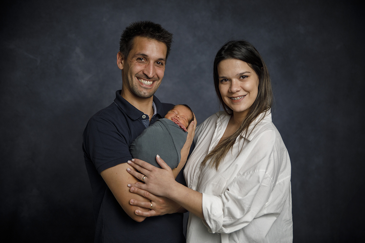 Os pais seguram o pequeno Gabriel ao colo enquanto ele dorme, ambos olham para a câmara de Foto Coimbra com sorrisos.