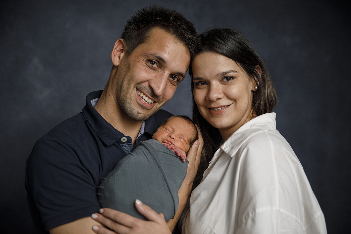 Num plano mais aproximado, do peito para cima, os pais seguram Gabriel enquanto ele dorme, ambos a sorrir para a câmara.