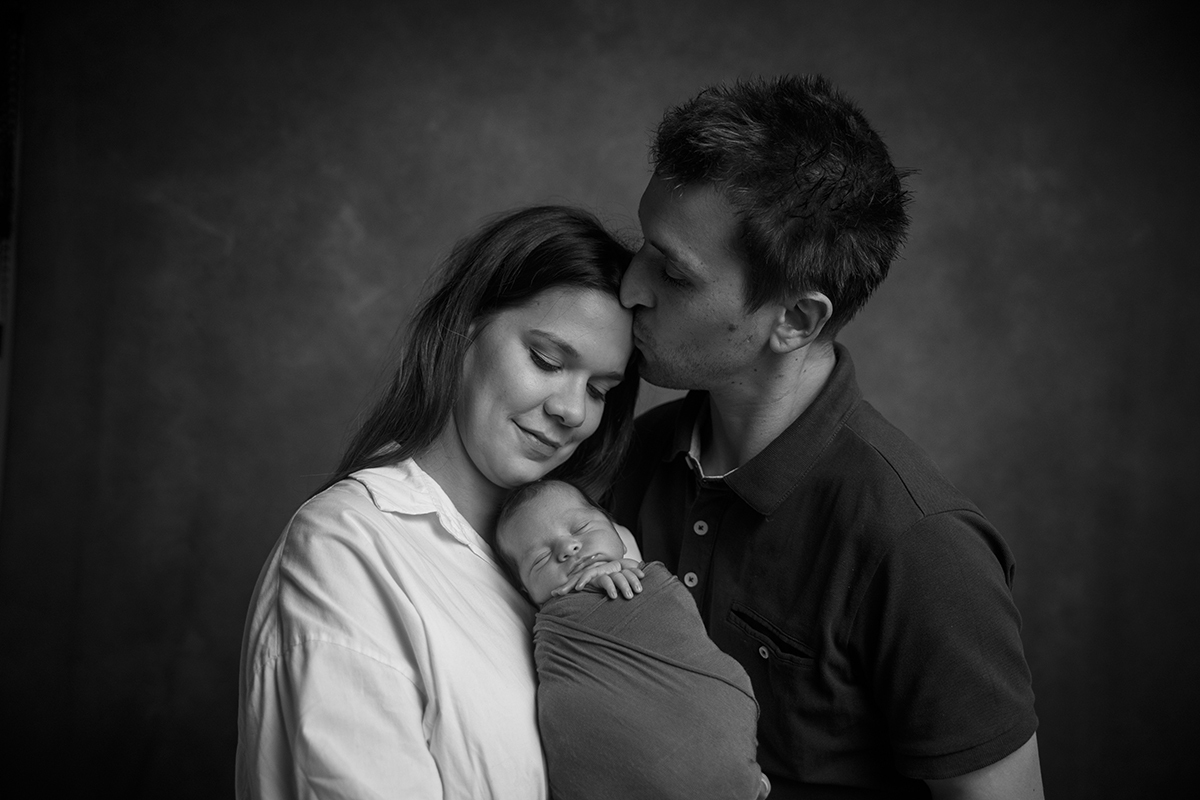 Também a preto e branco, agora com a mãe do lado esquerdo e o pai do lado direito da imagem, o pai beija a testa da mãe enquanto ela olha para Gabriel com um leve sorriso.