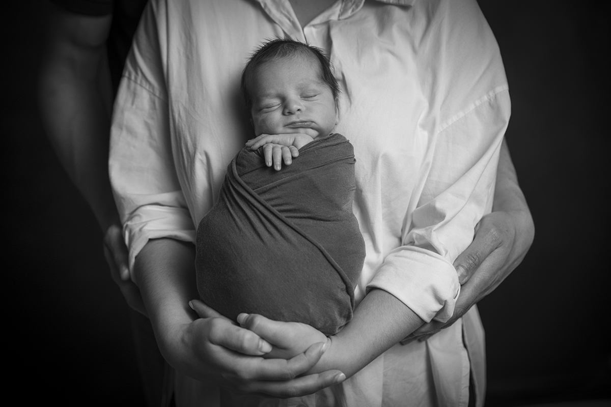A preto e branco, o pai está atrás a segurar nos braços da mãe que segura Gabriel enquanto ele dorme, uma foto incrível.