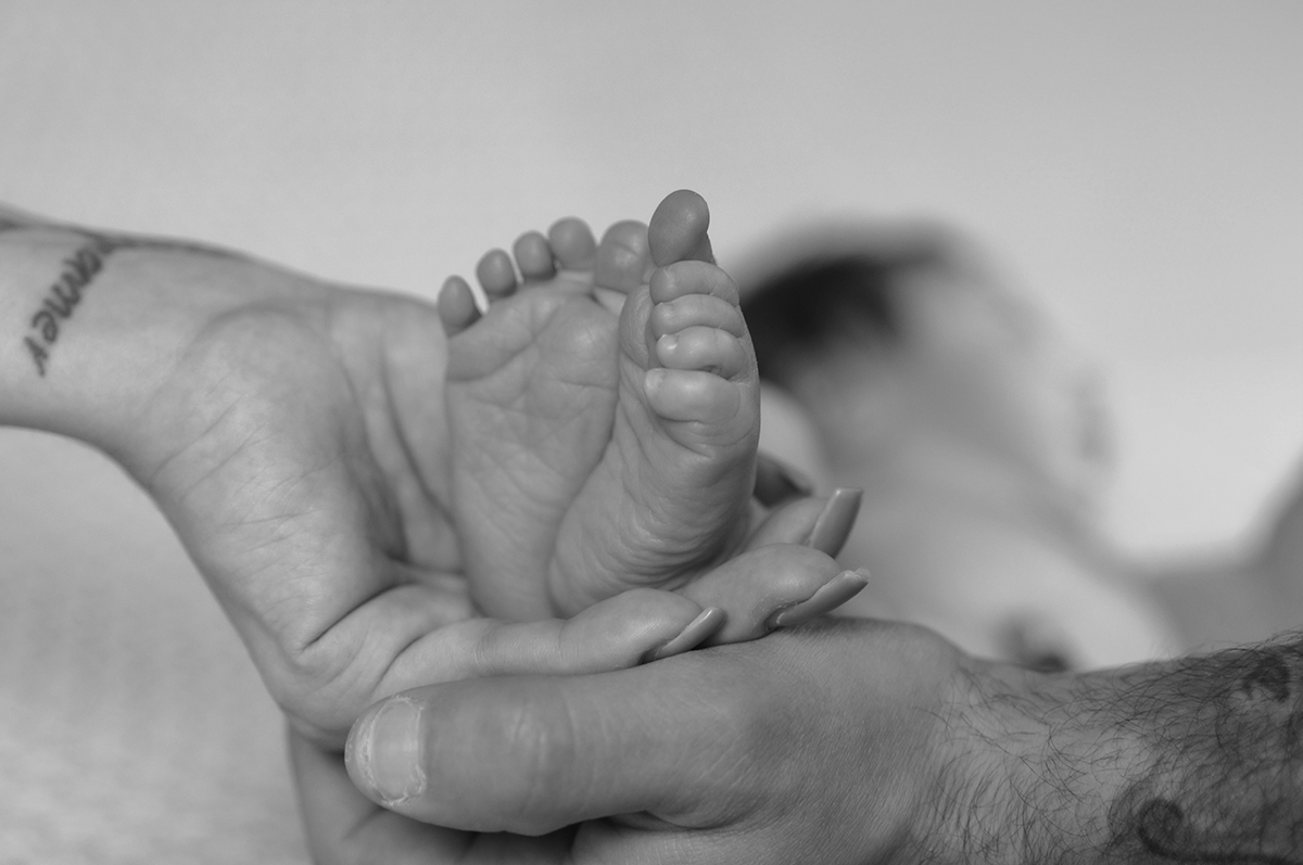 Foto a preto e branco que foca nas mãos dos pais a segurarem os pequenos pés de Lourenço. Um gesto simples, mas cheio de simbolismo.