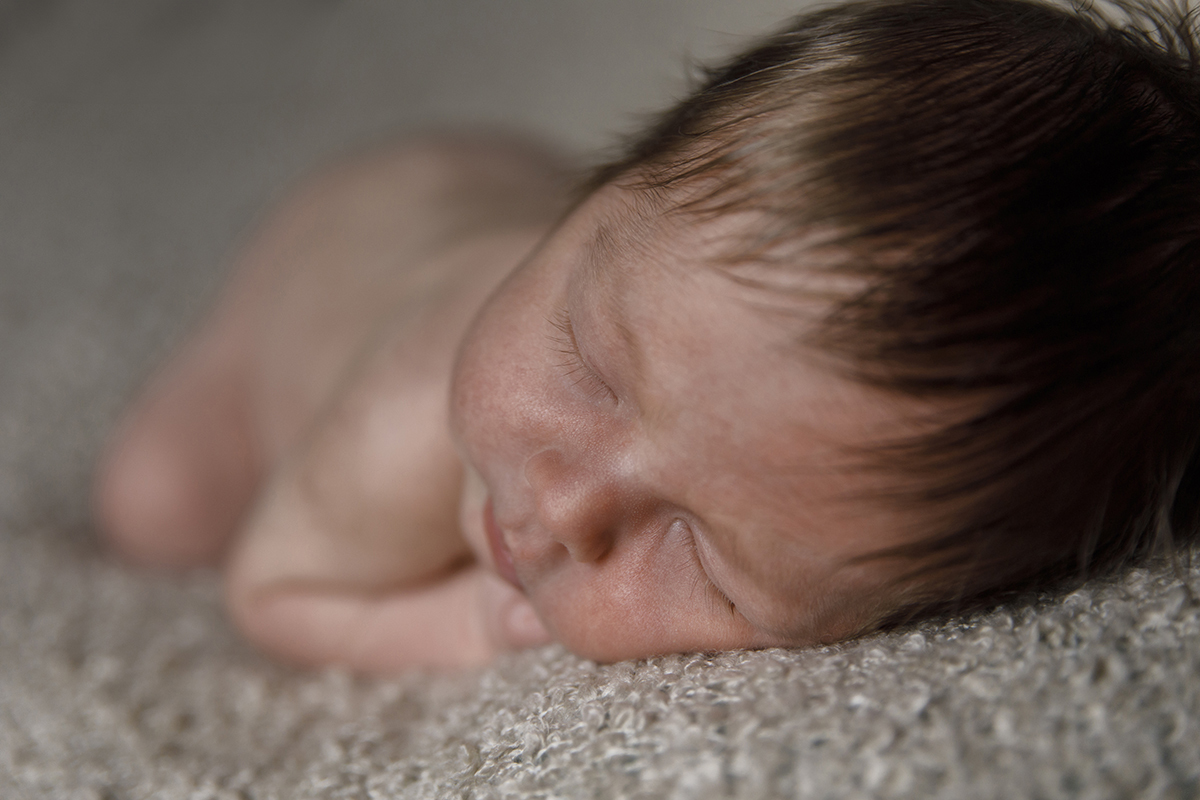 Agora num fundo bege, vemos Lourenço deitado de costas, nu, com o foco na cabeça e no cabelinho castanho. O corpo desfocado reforça o destaque no seu descanso tranquilo.