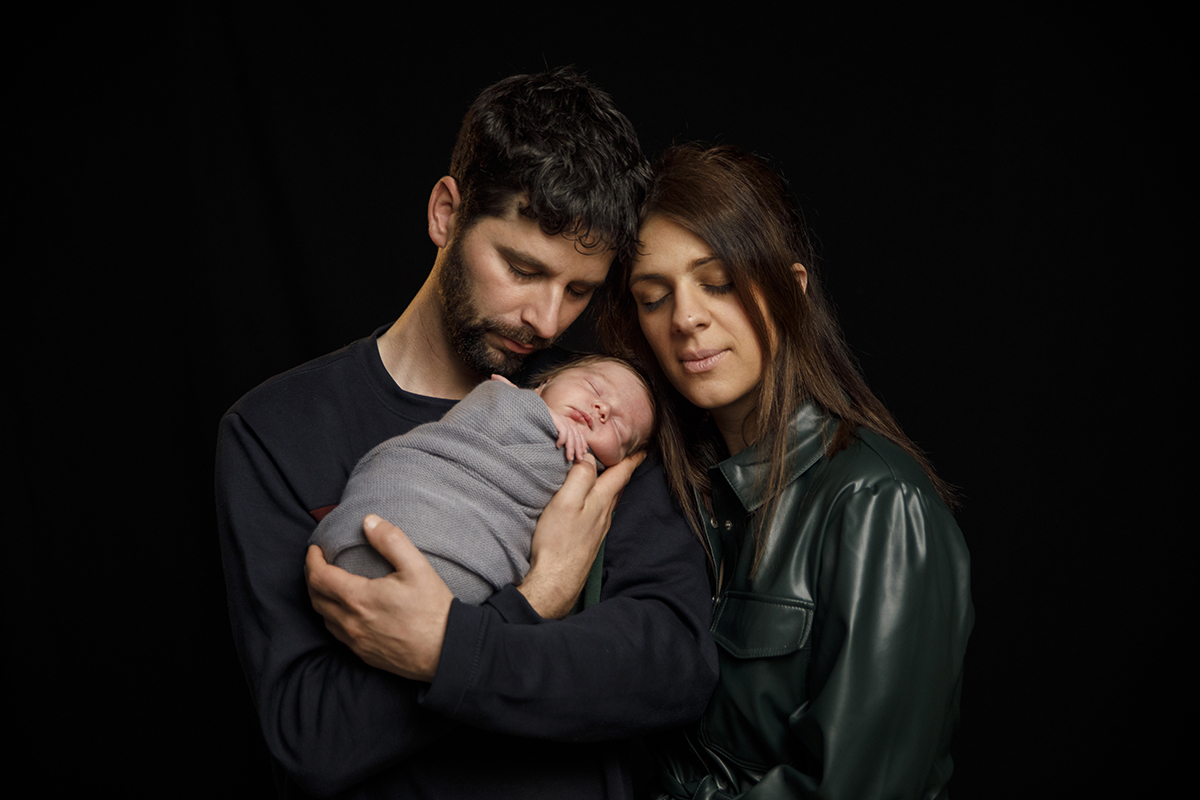 Contra um fundo preto, os pais de Lourenço seguram-no entre eles, encostando as suas faces à do bebé. Todos de olhos fechados, num momento íntimo e sereno.