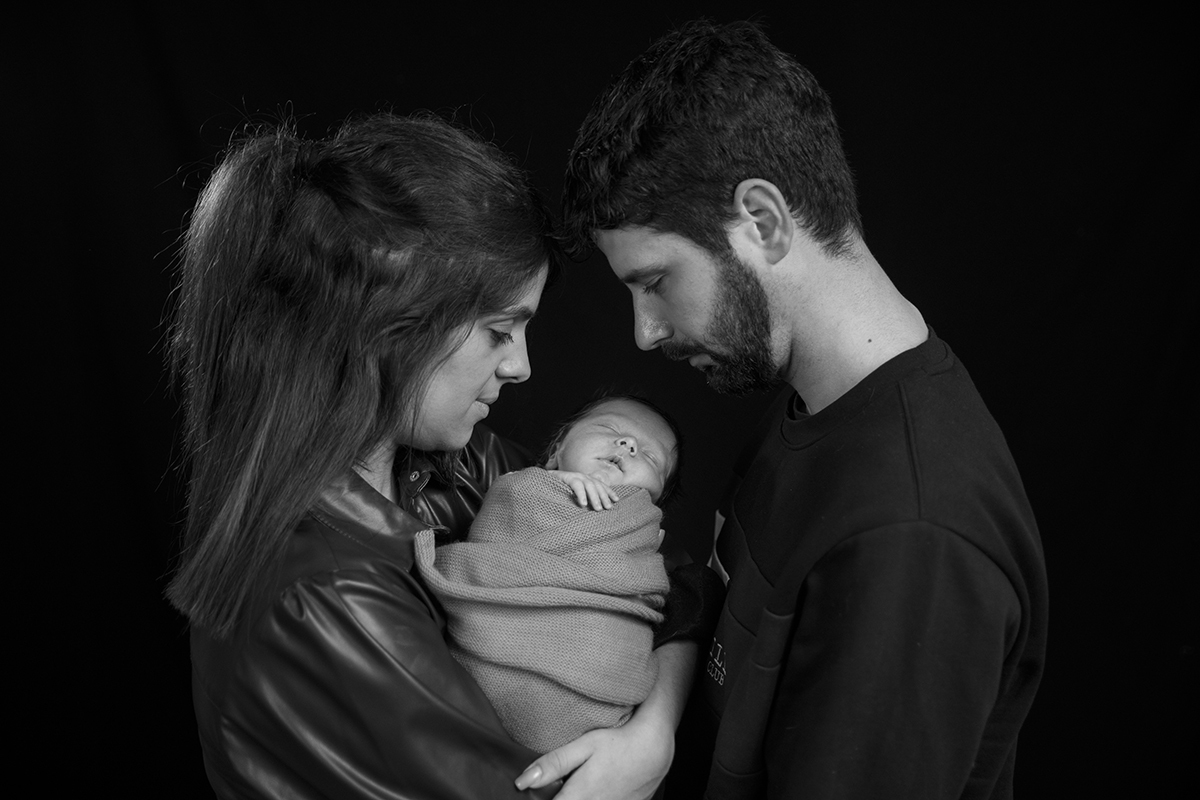 A preto e branco, a mãe à esquerda e o pai à direita, ambos em perfil, olham com carinho para Lourenço enquanto ele dorme entre eles.