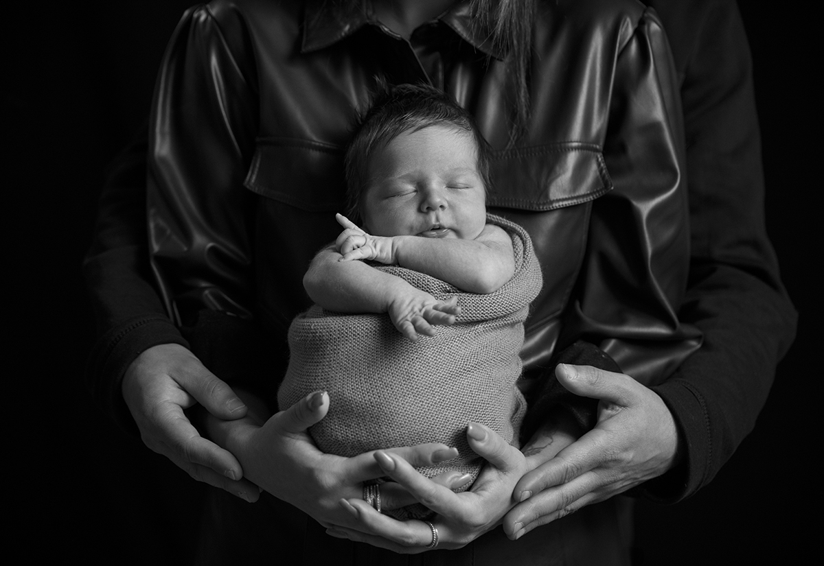 Ainda a preto e branco, Lourenço dorme enrolado na sua manta, com os braços de fora e um leve sorriso no rosto. A mãe segura-o, e o pai envolve-a por trás, num abraço cheio de significado. Fotografia bebe