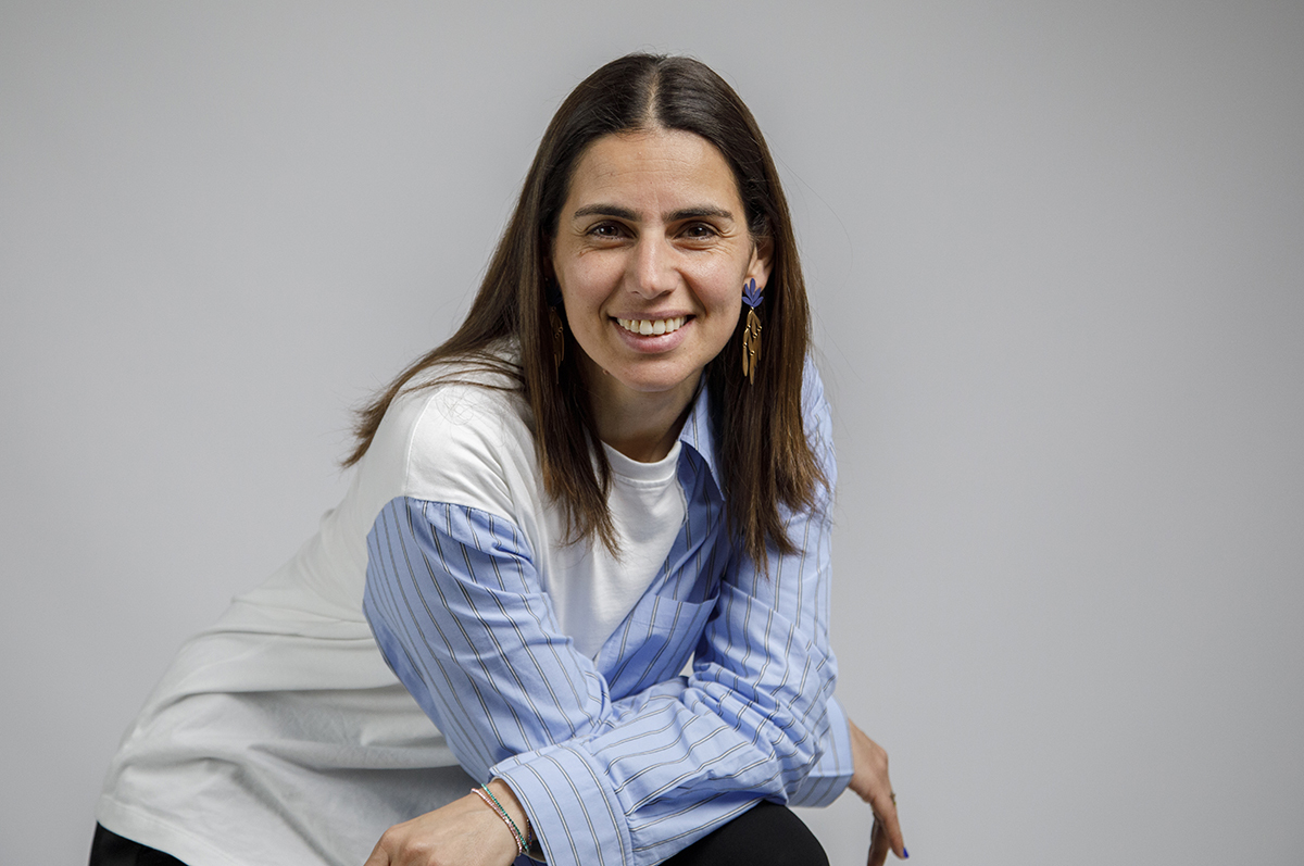 Neste retrato da cintura para cima, vemos Sónia com os braços cruzados apoiados sobre um joelho elevado, provavelmente devido a estar sentada. A ligeira inclinação para a frente e o sorriso espontâneo refletem conforto e autenticidade.