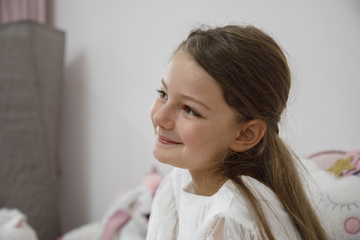 Num plano mais aproximado, Letícia sorri enquanto olha para o lado. A luz natural evidencia o brilho do seu olhar.
