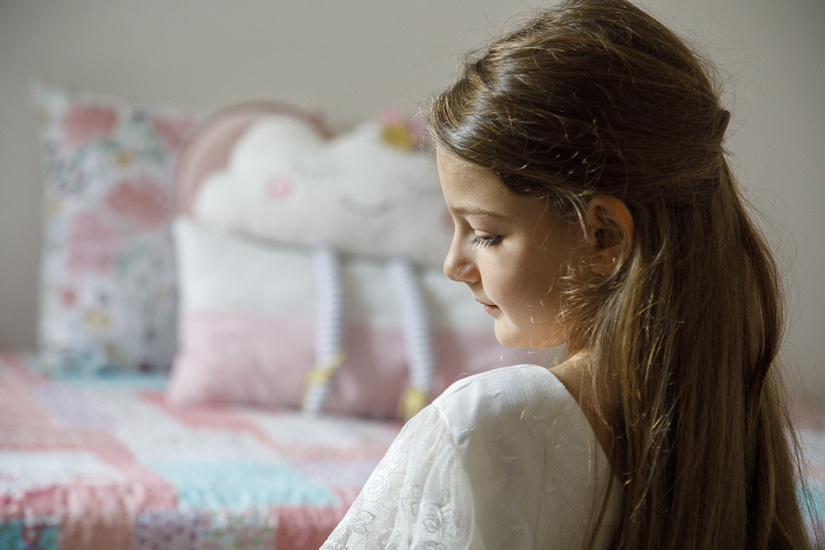 De costas e com o rosto parcialmente visível, Letícia parece refletir. A luz suave e o plano aproximado transmitem introspeção e doçura.