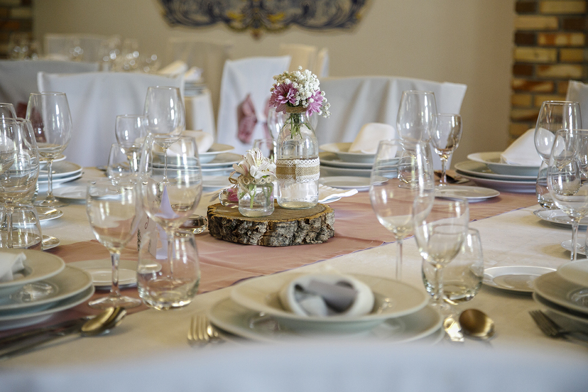 Num plano de detalhe, a mesa está decorada com dois pratos, dois copos de vinho e um de água, sobre um pano requintado. Simples e bonito.