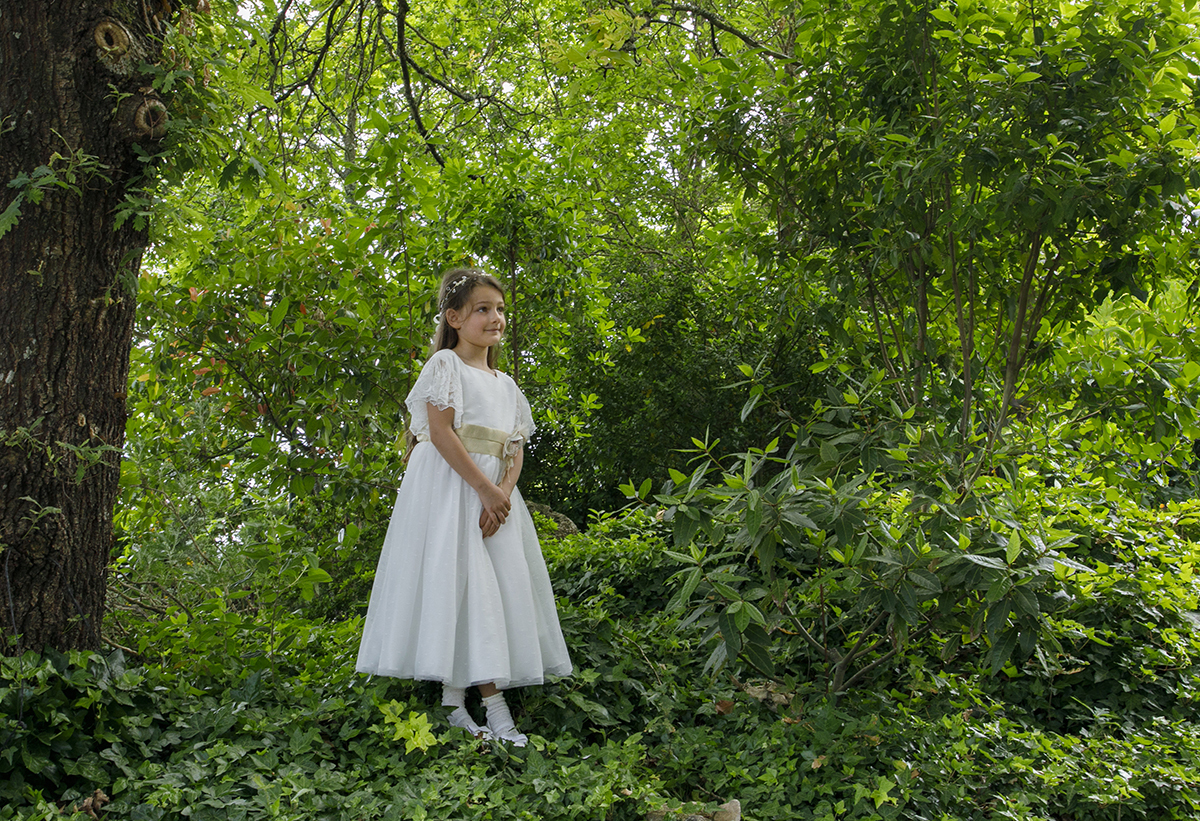 Ainda entre as trepadeiras, Letícia mantém as mãos juntas e sorri diretamente para a câmara, em plena sintonia com o ambiente.