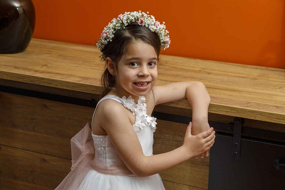 No mesmo cenário de madeira, Joana surge com um braço em cima do móvel e a outra mão a tocar na que cai, criando uma pose harmoniosa. Sorridente, deixa ver o laço rosa nas costas do vestido e os detalhes delicados da peça.