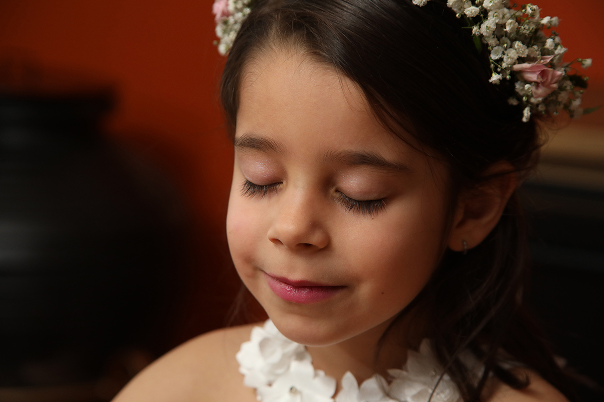 Num plano aproximado, com os olhos fechados e um leve sorriso, Joana transmite tranquilidade e felicidade. A sua coroa de flores está em destaque contra o fundo desfocado.