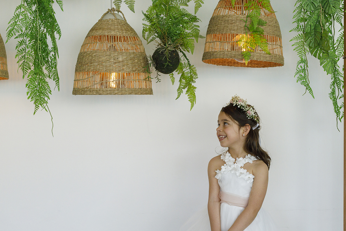 Joana está à direita da imagem, da cintura para cima, com a cabeça virada para os candeeiros de corda pendurados no teto entre plantas verdes. Um momento contemplativo e encantado. Quinta outeiro
