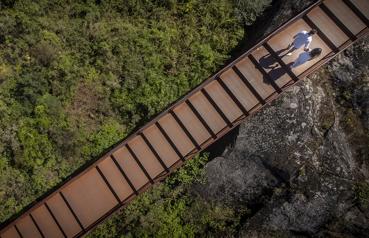De cima, veem-se as escadas e o casal de mãos dadas, a caminhar entre rochas e erva. Ricardo Coimbra Fotografo