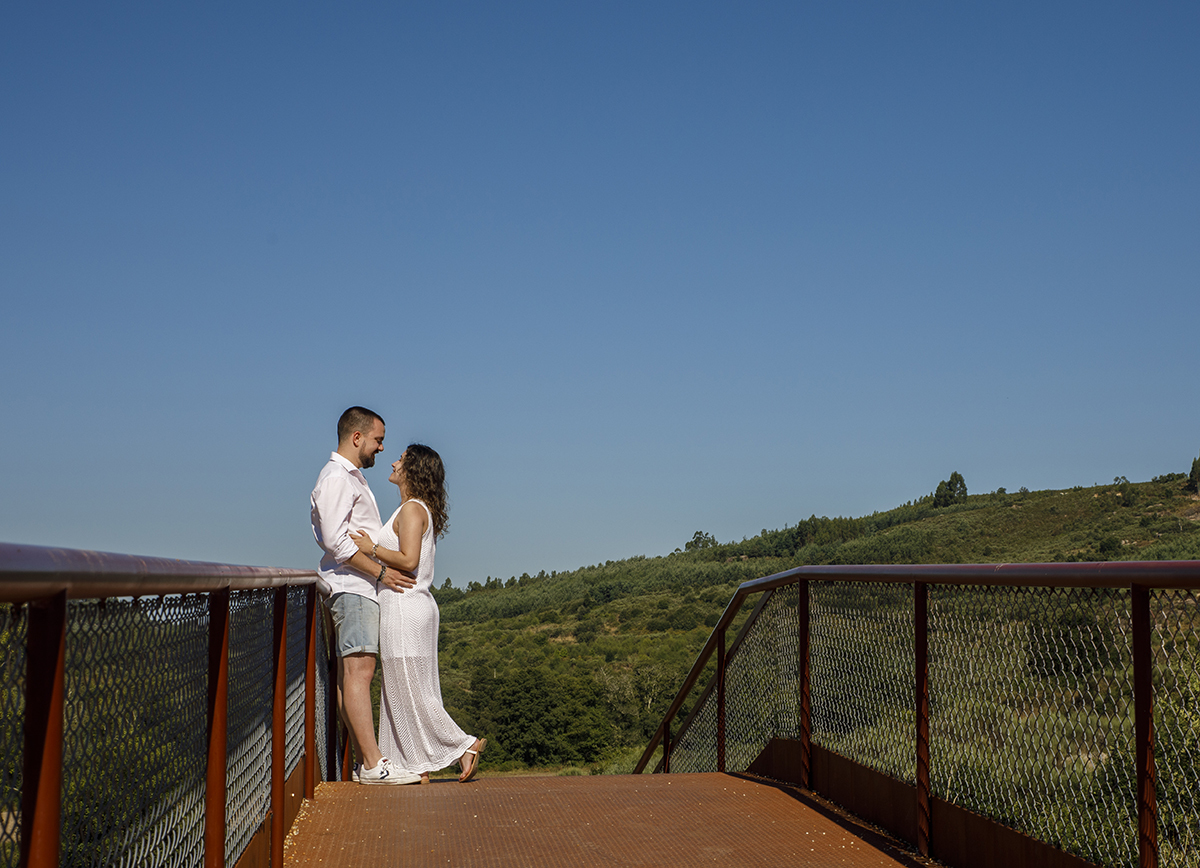 Abraçados no topo da ponte, trocam olhares doces, num instante em que o tempo parece parar.