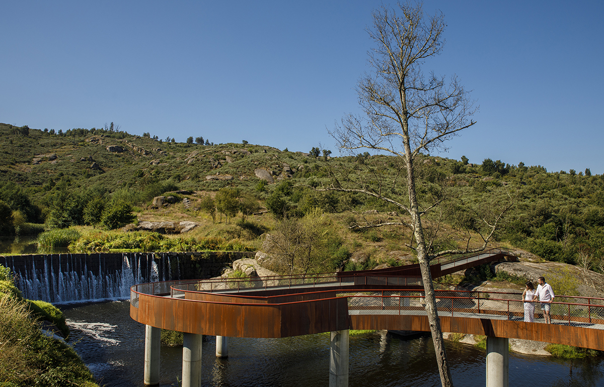 De mãos no varão, contemplam juntos a paisagem. A natureza abraça-os em silêncio.