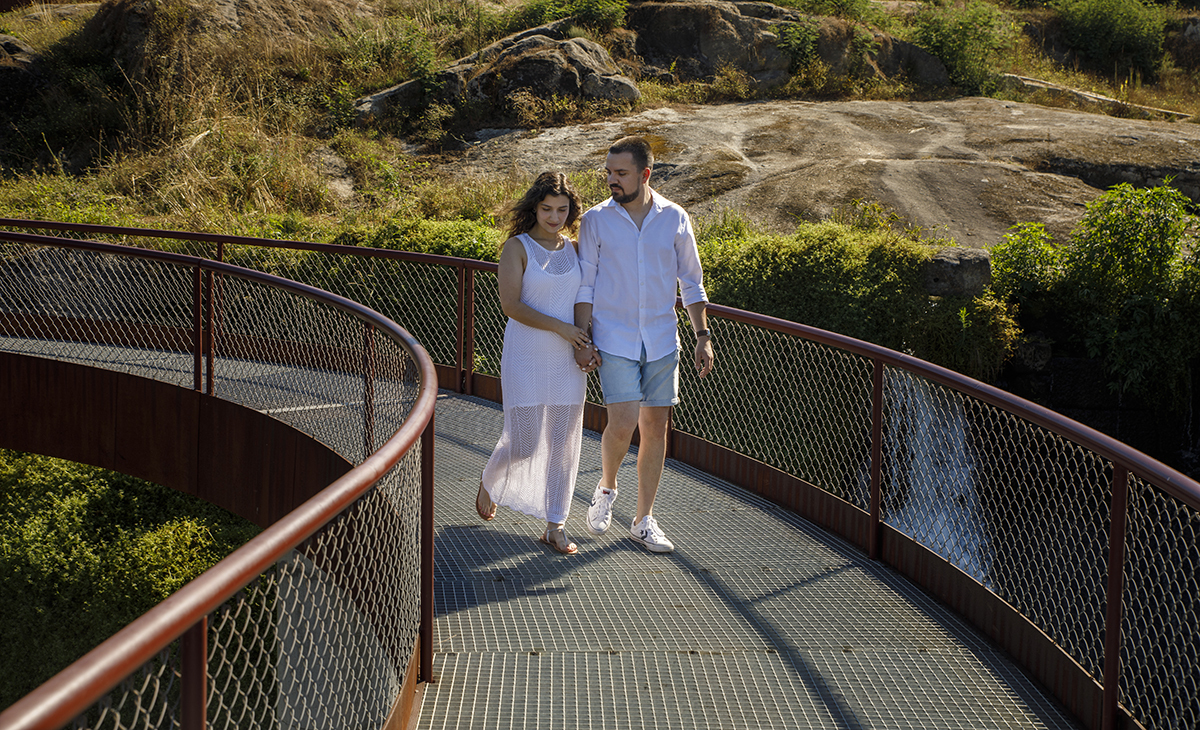 De mãos dadas, caminham pela ponte. Rafael olha para Sandra, que sorri para o chão.