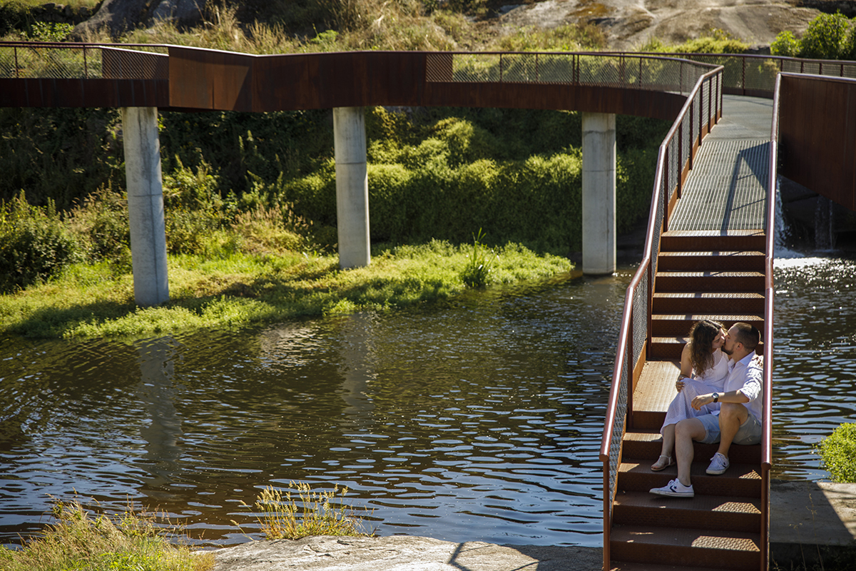 Sentados na escada da ponte, trocam um beijo com o rio a correr por baixo.