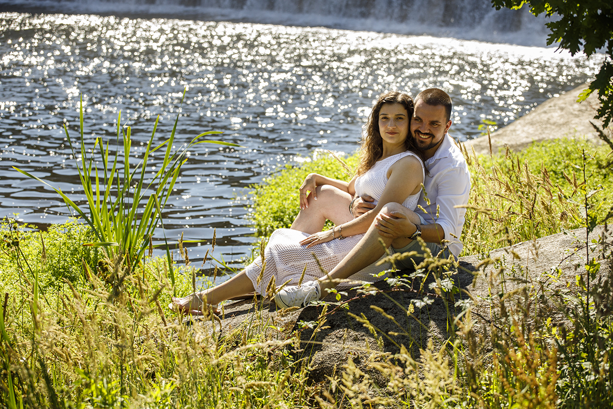 Sentados junto ao rio, Sandra olha para a lente, enquanto Rafael a envolve.